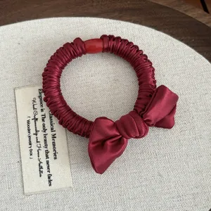 Close-up of burgundy pleated satin hair tie with a bow and red decorative bead