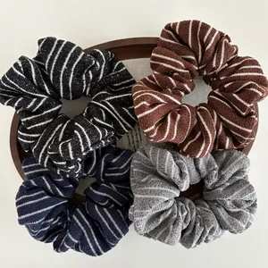 Close-up of four striped knit scrunchies displayed in a rustic wooden tray for hair styling