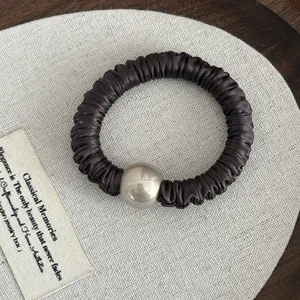 Detail of dark brown pleated satin hair scrunchie featuring a large metallic accent bead