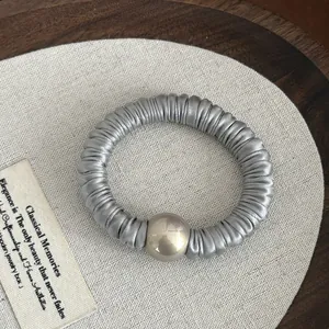 Detail of grey satin pleated scrunchie featuring a large champagne pearl bead on wood