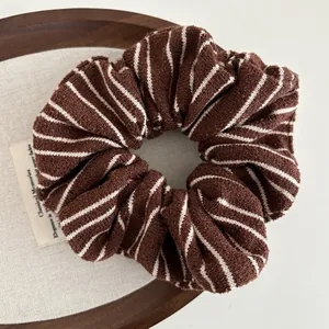 Detail of dark brown and white striped knit scrunchie on a wooden tray with soft lighting