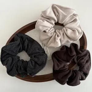 Three oversized thick wool scrunchies in grey, beige, and coffee on a wooden tray
