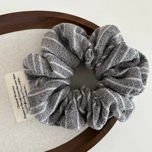 Detailed view of a soft grey and white striped knit scrunchie on a wooden tray