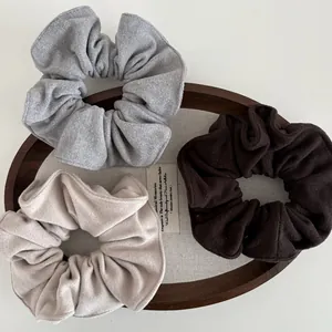 Close-up of three large wool-textured scrunchies in grey, cream, and brown on a wooden tray