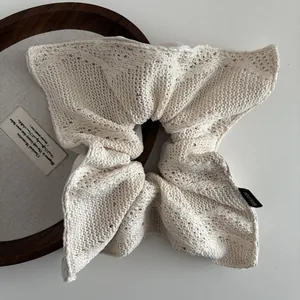 Detail van beige gebreide scrunchie met lovertjes en Hand Made-label op hout