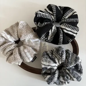 Dettaglio di tre elastici in maglia beige, nero e grigio con etichette 'Hand Made' cucite