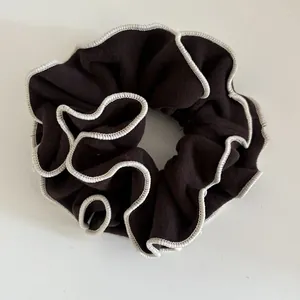 Close-up of dark brown wool scrunchie featuring decorative white stitched edges and ruffles