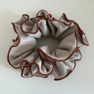 Macro detail of grey suede scrunchie with brown stitched edges and wavy pleats