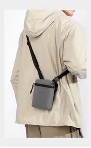 Rear view of a model wearing a grey nylon crossbody bag with adjustable strap and zip pocket