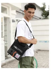 Detail showing the adjustable wide strap and orange zipper pulls on the black outdoor bag