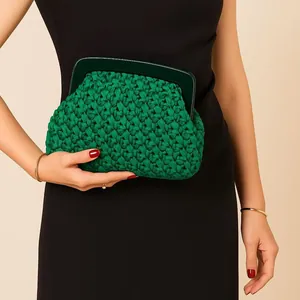 Close-up of an elegant green woven clutch bag with acrylic frame held by a model