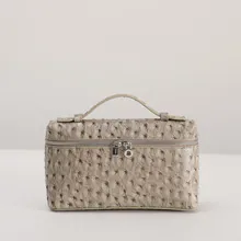 Close-up of ostrich pattern leather texture and silver dual zippers on the beige vanity bag