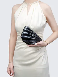 Detail of elegant black shell-shaped acrylic clutch bag held with a white evening dress
