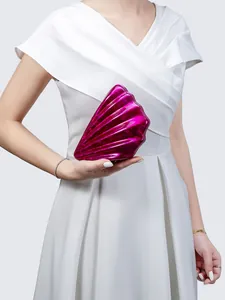 Detail shot of a bright fuchsia shell-shaped acrylic clutch bag held by a model