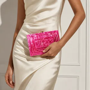 Detail view of a hot pink marbled acrylic clutch bag held by a model in a satin dress