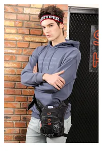 Detail of a tactical drop leg bag in black with orange accents on a textured brick background