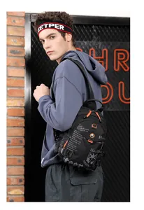Detail of waterproof black nylon crossbody bag with orange zipper pull on industrial wall
