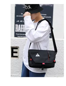 Close-up of black waterproof messenger bag with red strap buckle and white logo detail