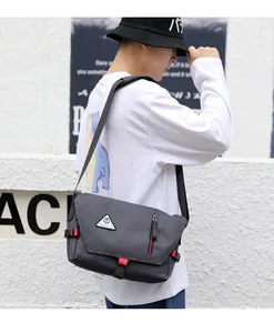 Side view of dark grey waterproof messenger bag with red accents on male model