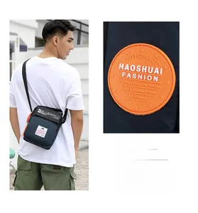 Détail du sac bandoulière en nylon bleu marine avec badge orange et sangle ajustable