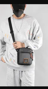 Detail of waterproof nylon crossbody bag featuring grey fabric and orange logo accents