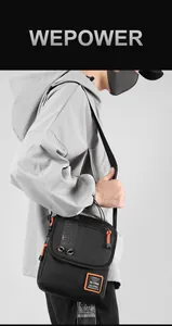 Men's black tactical crossbody bag with orange zipper details on model wearing grey hoodie