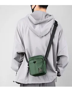 Detailed view of dark green nylon mini crossbody bag worn by model over a grey hoodie