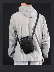 Vista detallada de un bolso bandolera camuflaje negro para hombre en chaqueta gris