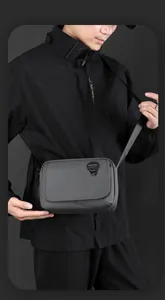 Close-up of a men's grey waterproof nylon crossbody bag with logo detail on front flap