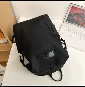 Minimalist black waterproof backpack with tactical hooks and artistic label on a white desk