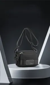 Detail of black nylon crossbody bag with multi-zipper pockets on a white podium