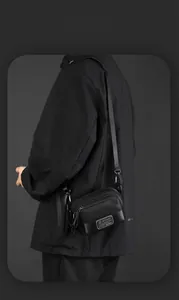 Detail of a minimalist black nylon men's crossbody bag with multiple zipper compartments