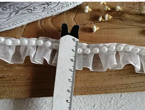 Detail of 2cm white pleated organza lace trim with beads against a dark wood surface