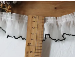 Detail of 5.5cm white pleated lace trim with black contrast stitching on wood ruler