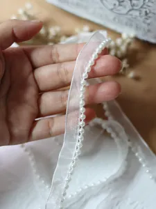 Macro detail of white organza ribbon with pearl beads for garment sewing and DIY crafts