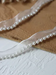 Macro shot of white organza ribbon trim with elegant faux pearl beading for DIY sewing