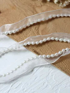 Macro detail of white organza lace ribbon with beaded pearls for DIY dress trimming