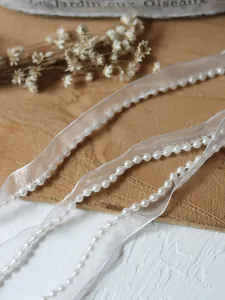 Close-up of white faux pearl beads on translucent organza ribbon for dress trim