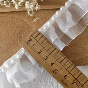 Detail von weißer plissierter Organza-Spitze mit Perlen für die DIY-Kleiderdekoration