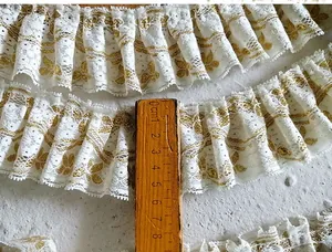 Detail view of 4cm wide white pleated lace with gold embroidery and ruffled texture