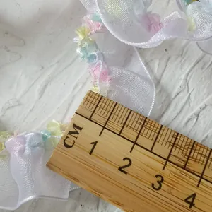Close-up of 2cm wide white pleated mesh lace with colorful pastel frayed edges and ruler