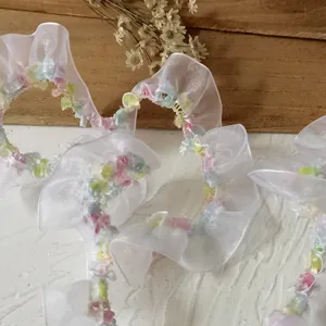 Close-up of 2cm white ruffled organza lace trim with colorful floral embroidery details