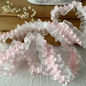 Dettaglio del bordo in pizzo plissettato a doppio strato in raso rosa e organza bianca