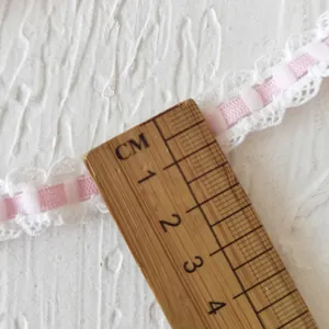 Pink checkered ribbon with white lace trim and wooden ruler measuring width