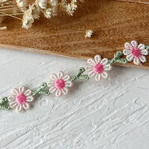 Close-up of white and pink embroidered daisy lace trim with green leaf embroidery