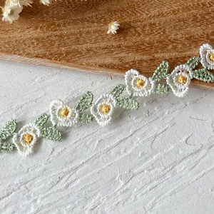 Close-up of embroidered white daisy lace ribbon with green leaves on wooden surface