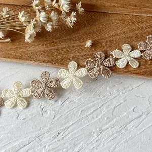 Detailed close-up of cream and khaki embroidered daisy lace trim on a rustic background