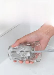 Detail of long-handle sponge brush creating rich foam inside a glass cup for cleaning