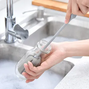 Ergonomic long handle sponge bottle brush cleaning a glass bottle with foam in a sink