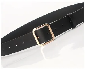 Detail of a minimalist black PU leather belt featuring a polished gold square buckle